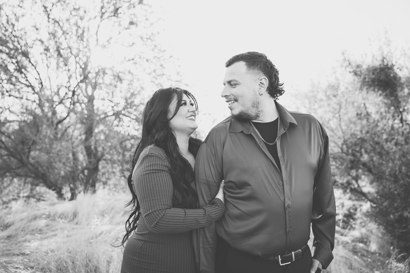 Engaged couple looking at each other and smiling, coloring is black and white.