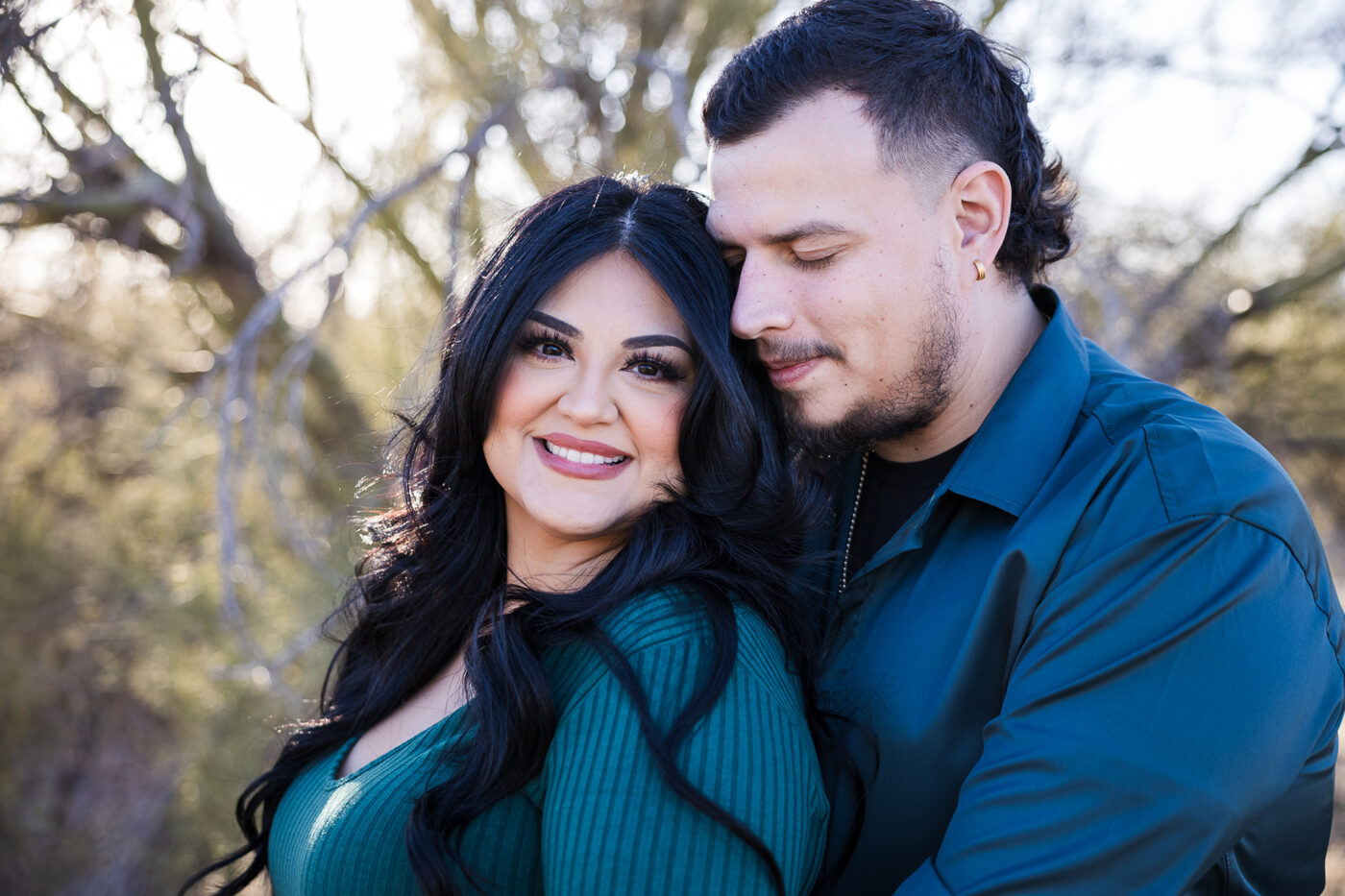 Close up on engaged couple, she's looking at the camera smiling and he's looking down with his face in her hair.