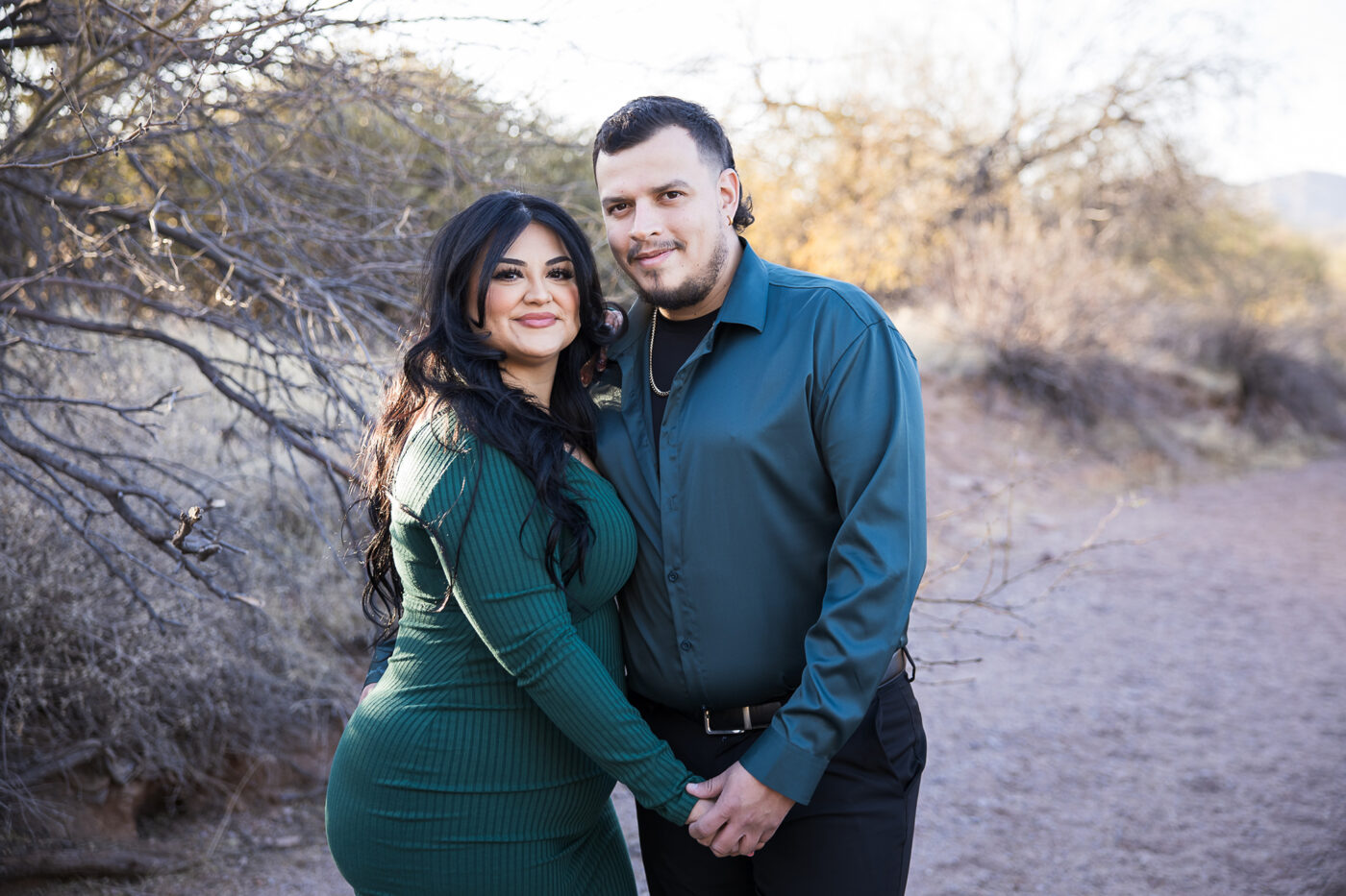 Engaged woman wearing deep green holding hands with her fiance wearing teal in a desert wash. 