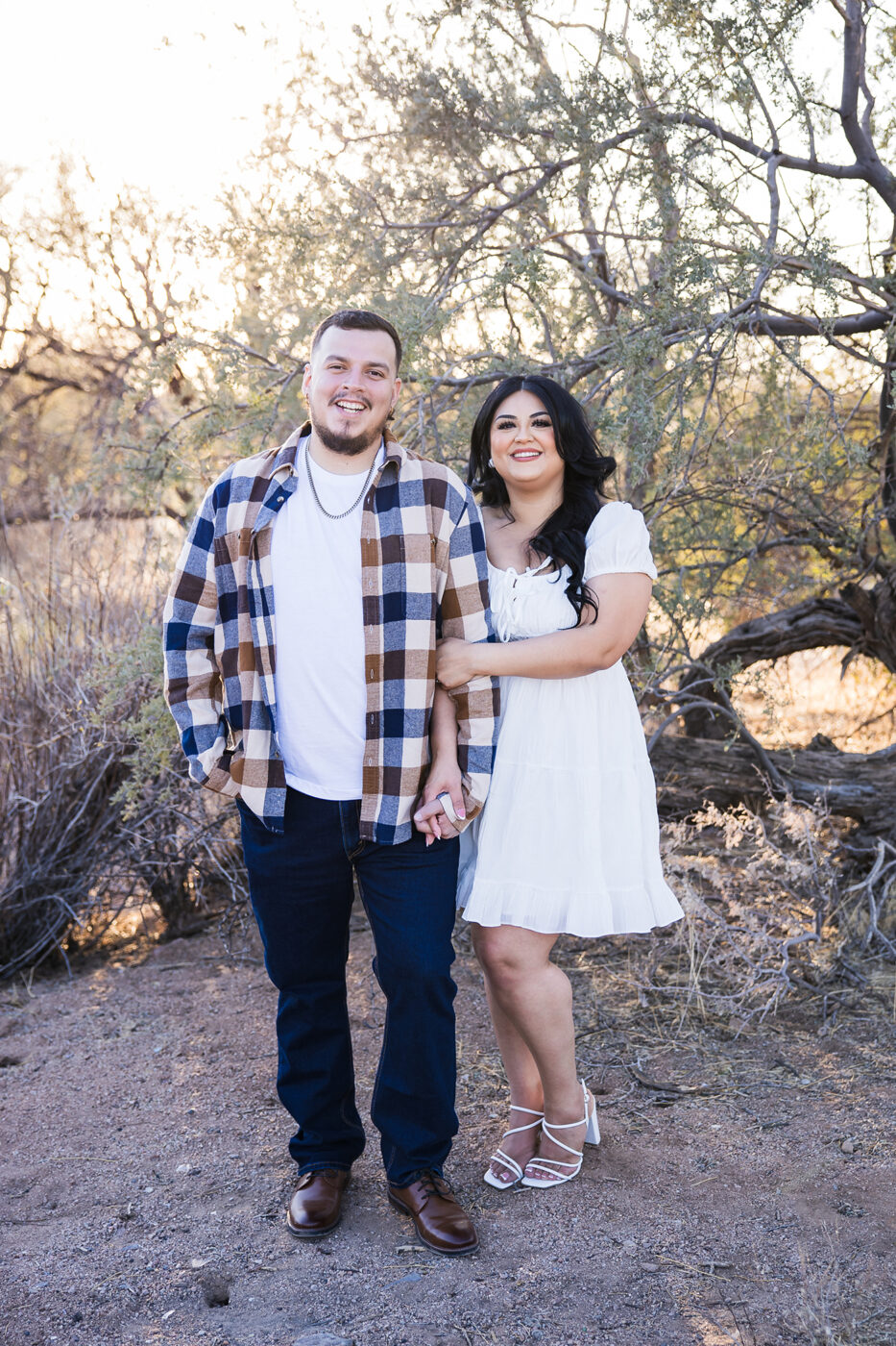 Engaged couple in the desert looking at the camera smiling.