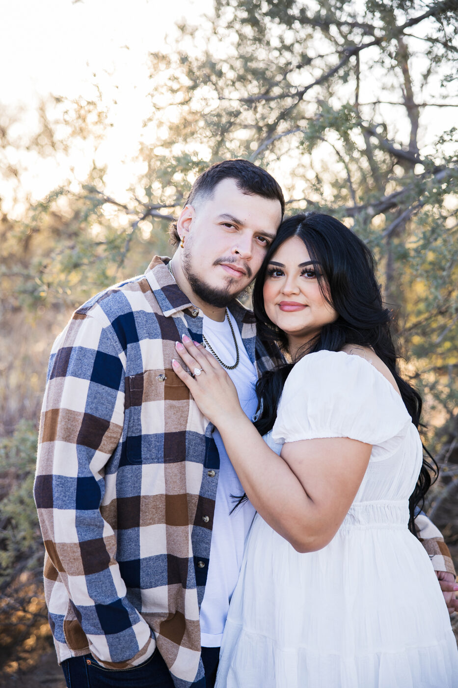 Close up of couple looking at the camera, she's showing off her ring on his chest.