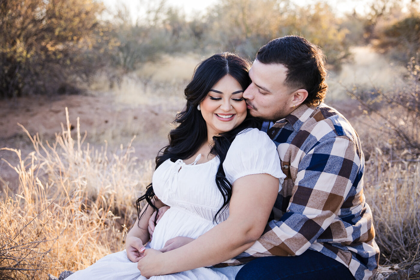 Couple sitting together with his arms around her and they are turned towards each other grinning.