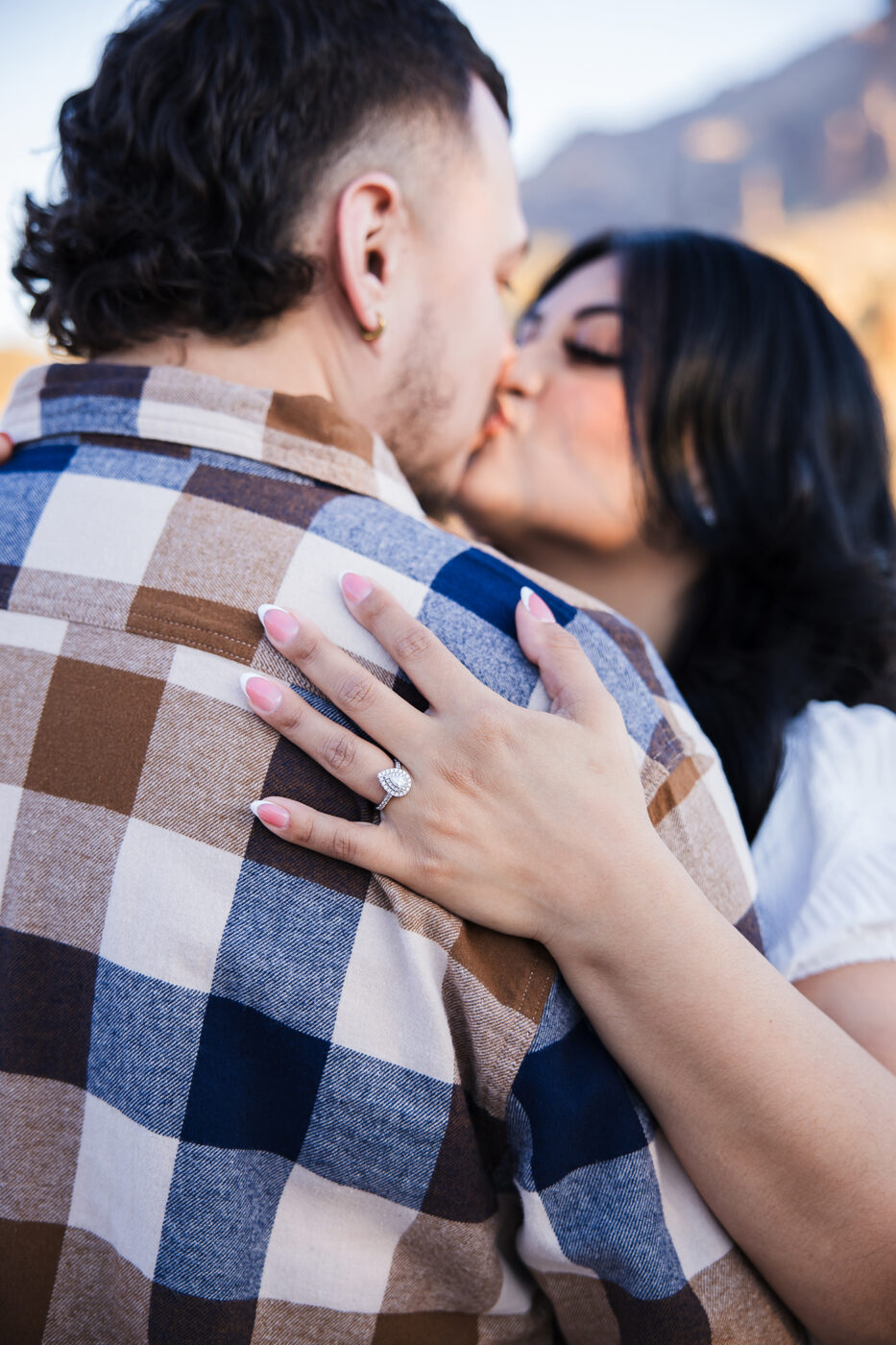 Close up of woman's ring on her fiance's back while they are kissing.