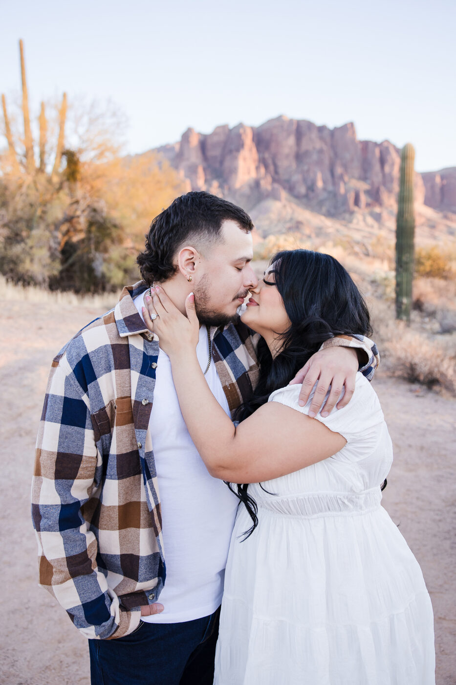 Gorgeous couple with dark hair close to kissing with their arms around each other with Superstition Mountain in the background.