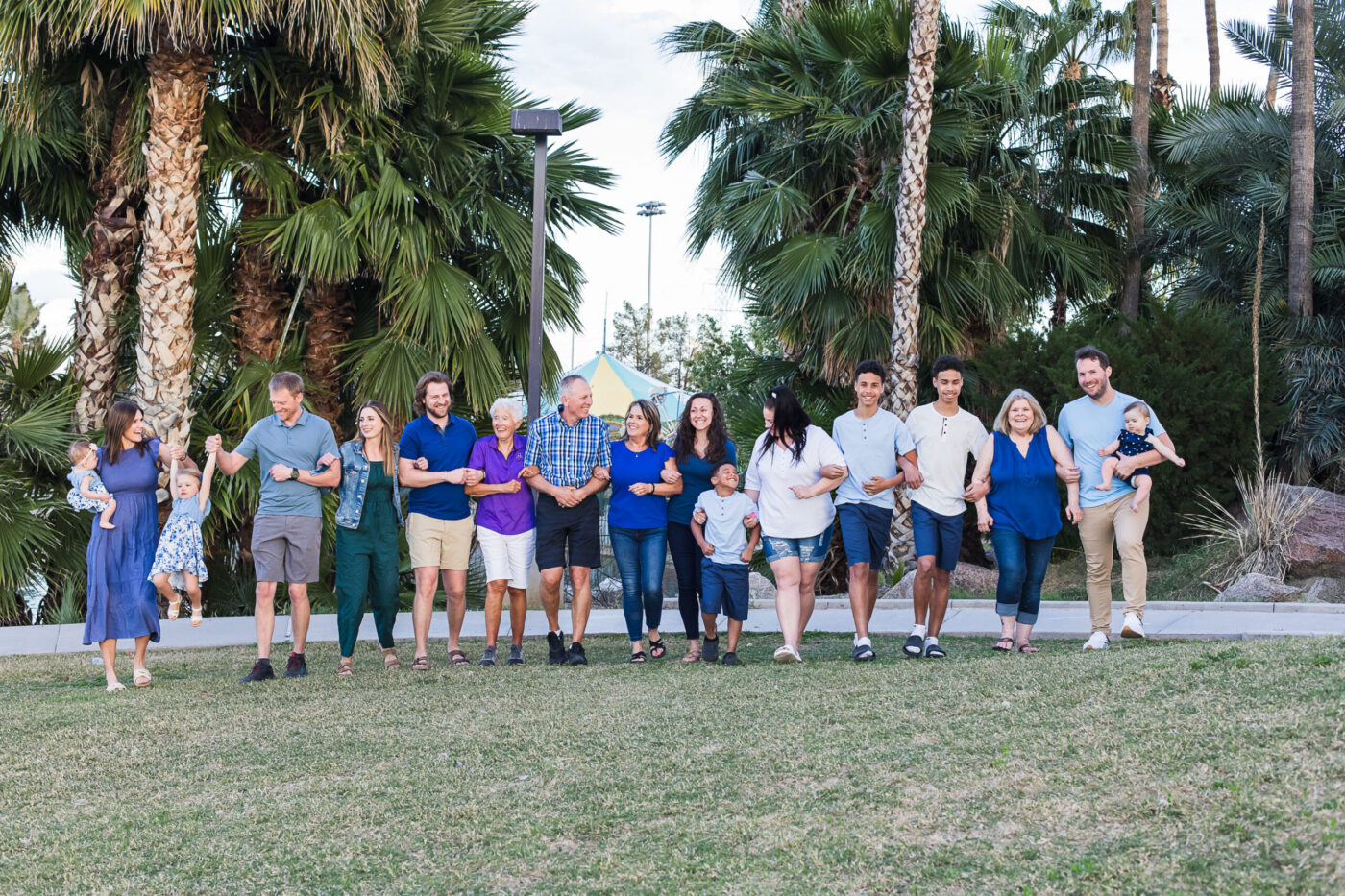Large extended family all walking together arm in arm through grass.