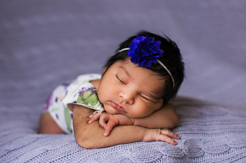 Sleeping newborn girl laying on her stomach on a purple background.