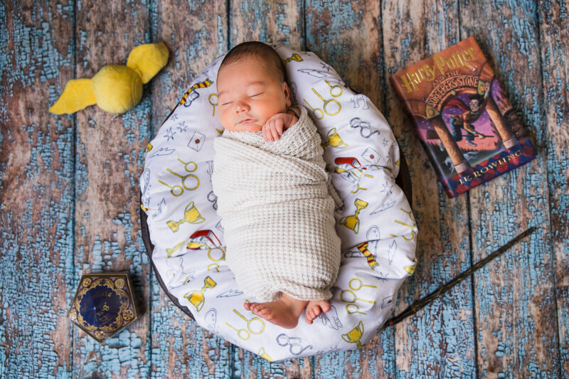Newborn baby boy in a bowl surrounding by Harry Potter props.