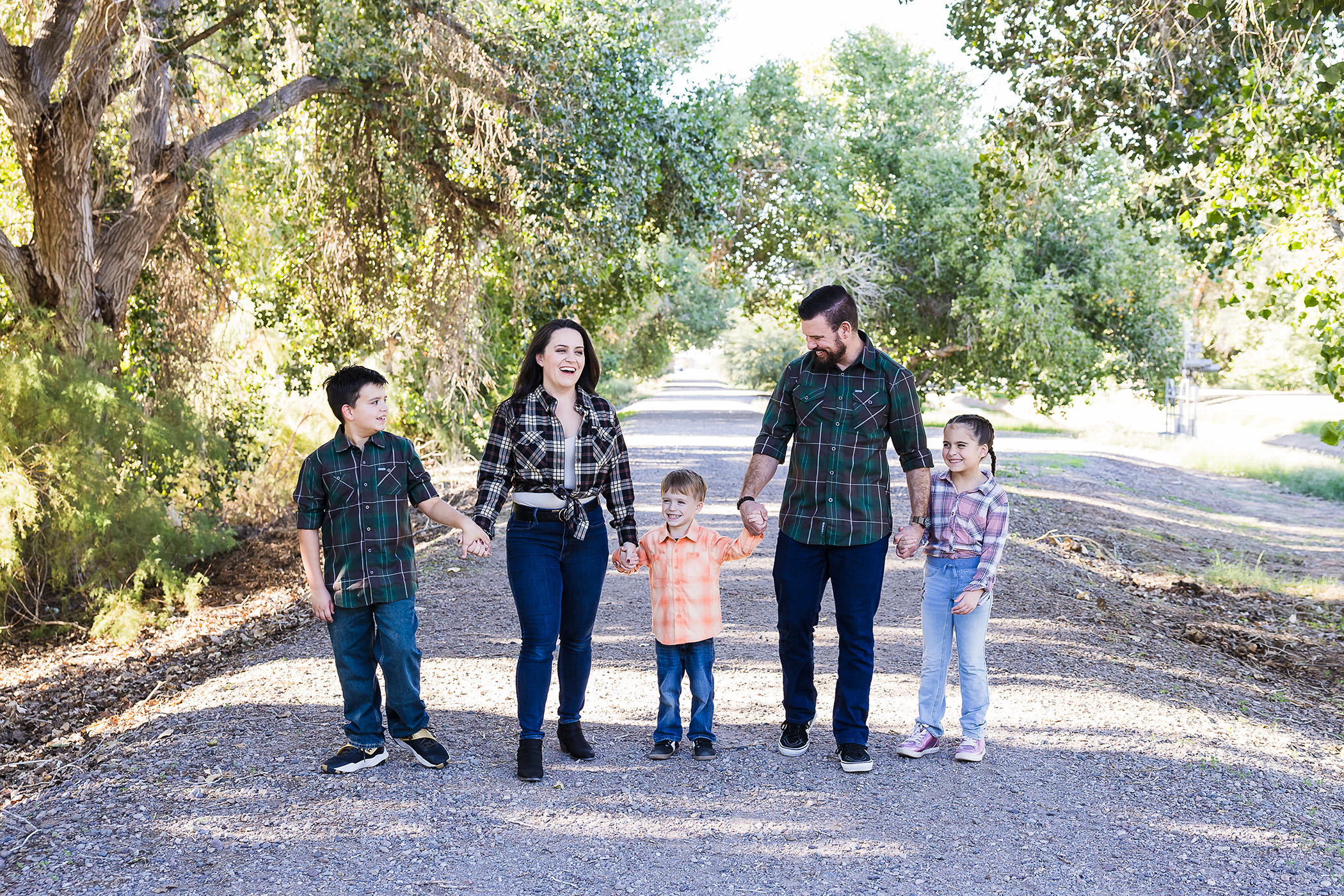Family of five in plaid walking and smiling together in a tree area.